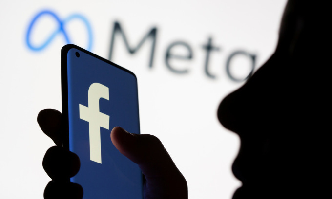 Một người cầm điện thoại với biểu tượng Facebook và công ty mẹ Meta. Ảnh: Reuters.